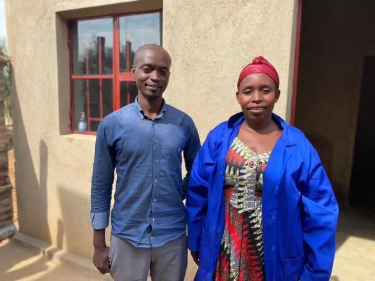 Clémence Murekatete yambaye itaburiya y’ubururu ahagaze mu nzu y’inkoko ze,